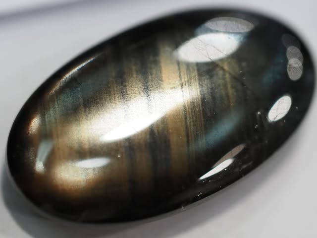 Oval gold sheen sapphire cabochon with dark and gold banding, studio photograph on white