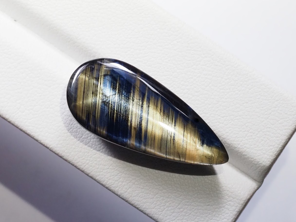 Polished gold sheen sapphire cabochon in a teardrop cut, showing banded blue and gold chatoyancy